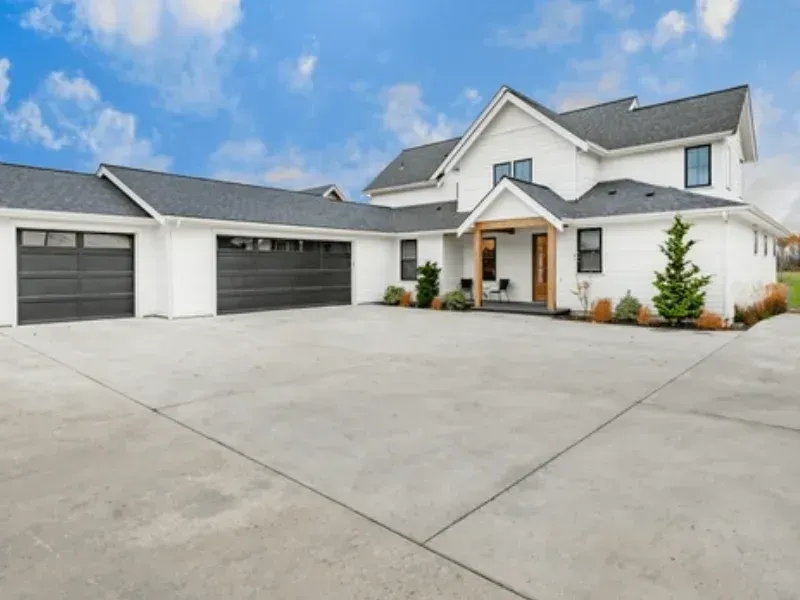 Modern white two-story house with a large concrete driveway and two garage doors under a blue sky
