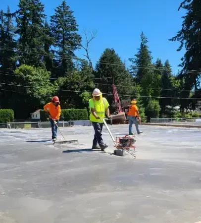Construction workers smoothing a concrete slab with power trowels on a sunny outdoor site.