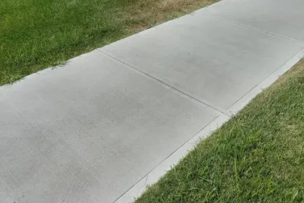 A straight, light grey concrete sidewalk bordered by green grass on both sides.