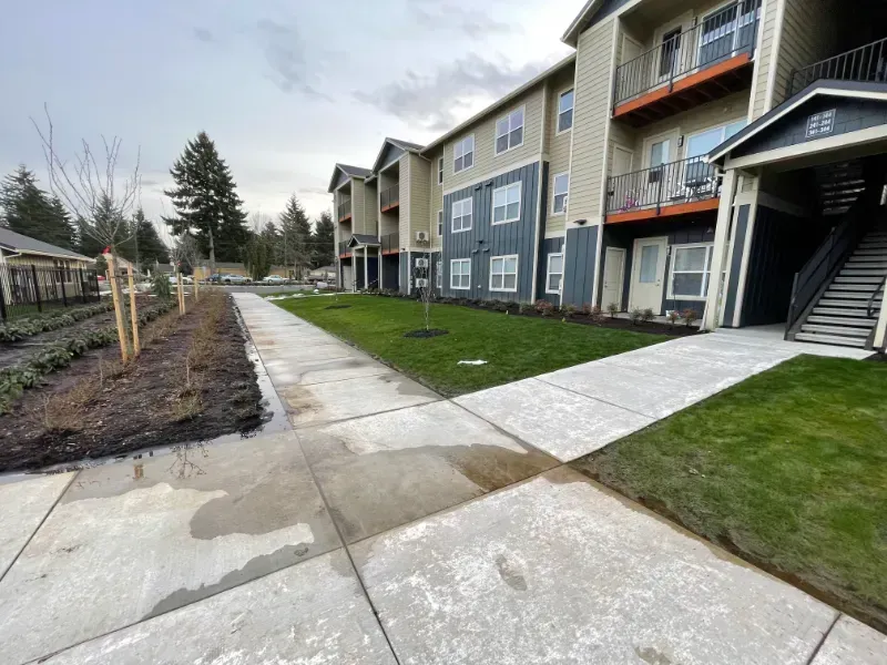 Apartment walkway and stairs beside blue-gray townhomes, with grass and a landscaped path on a cloudy day