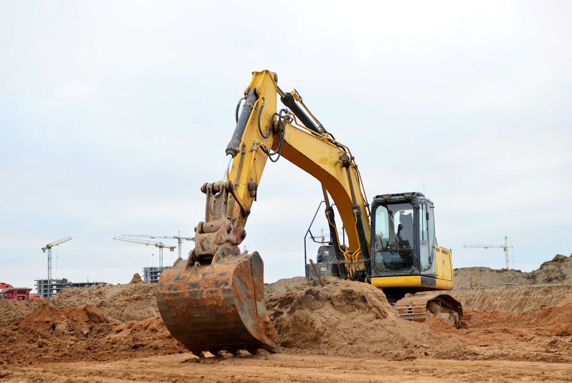 Une excavatrice jaune déplace de la terre sur un chantier de construction.