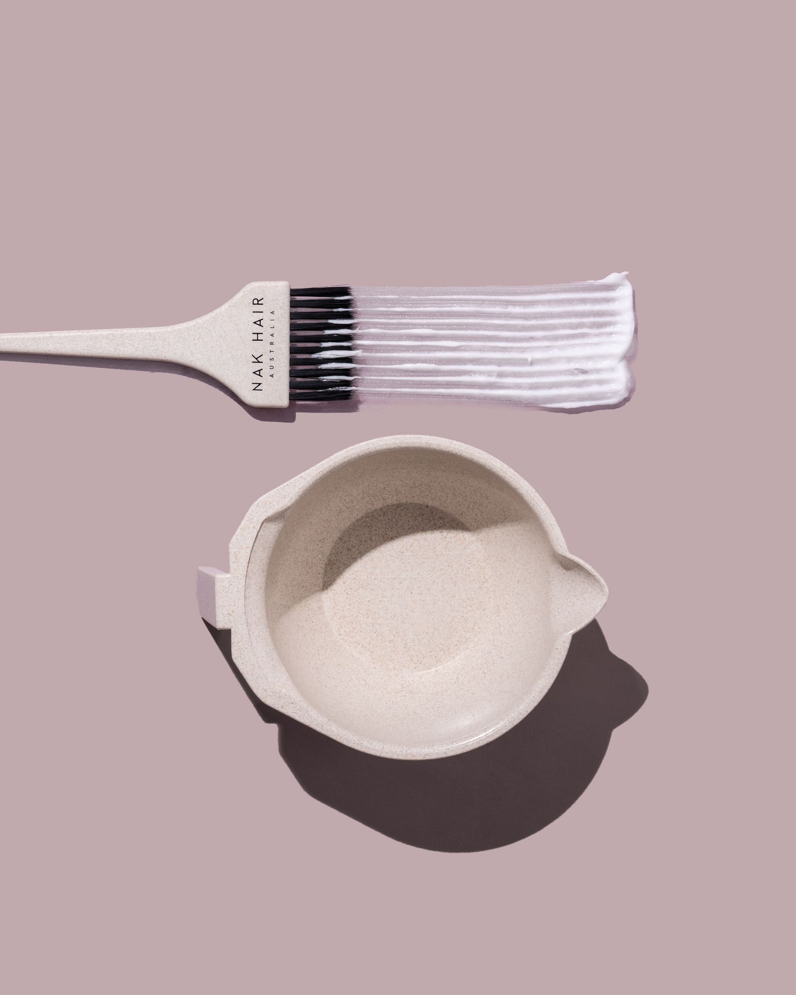 A brush and a bowl of hair dye on a pink background — Lavie Hair & Beauty in Ciccone, NT
