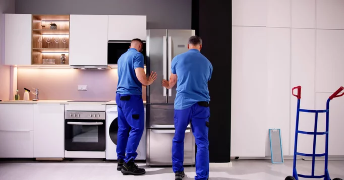 Two men are working on a refrigerator in a kitchen.