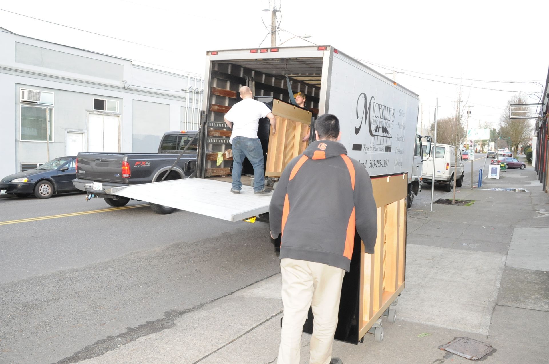 A man is pushing a piano out of a movers truck
