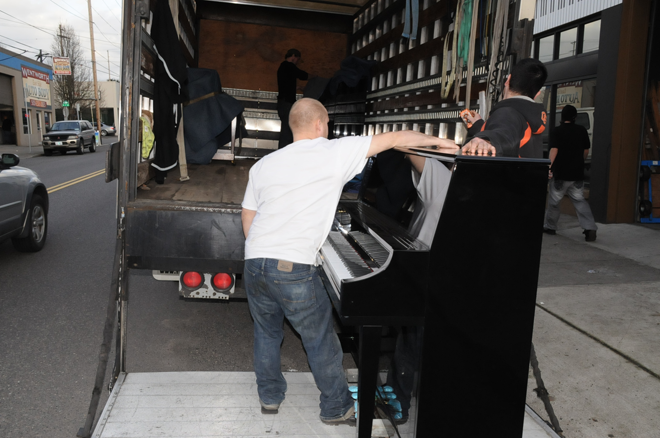 A man is pushing a piano out of a truck