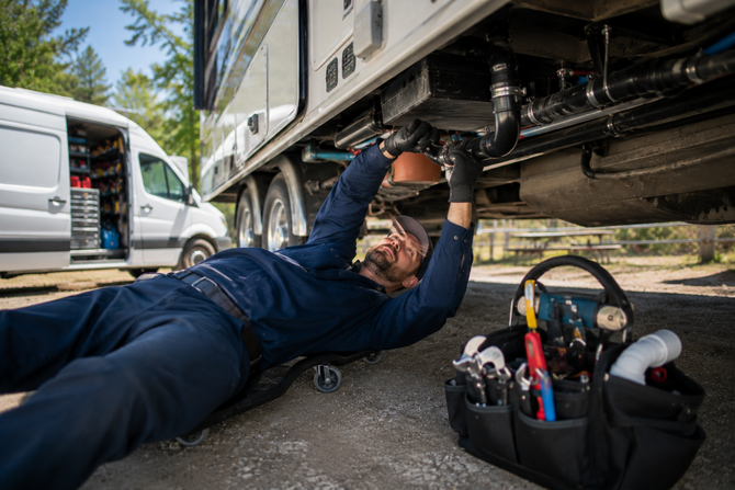 Mechanic lying under a truck, working overhead beside a tool bag and open van.