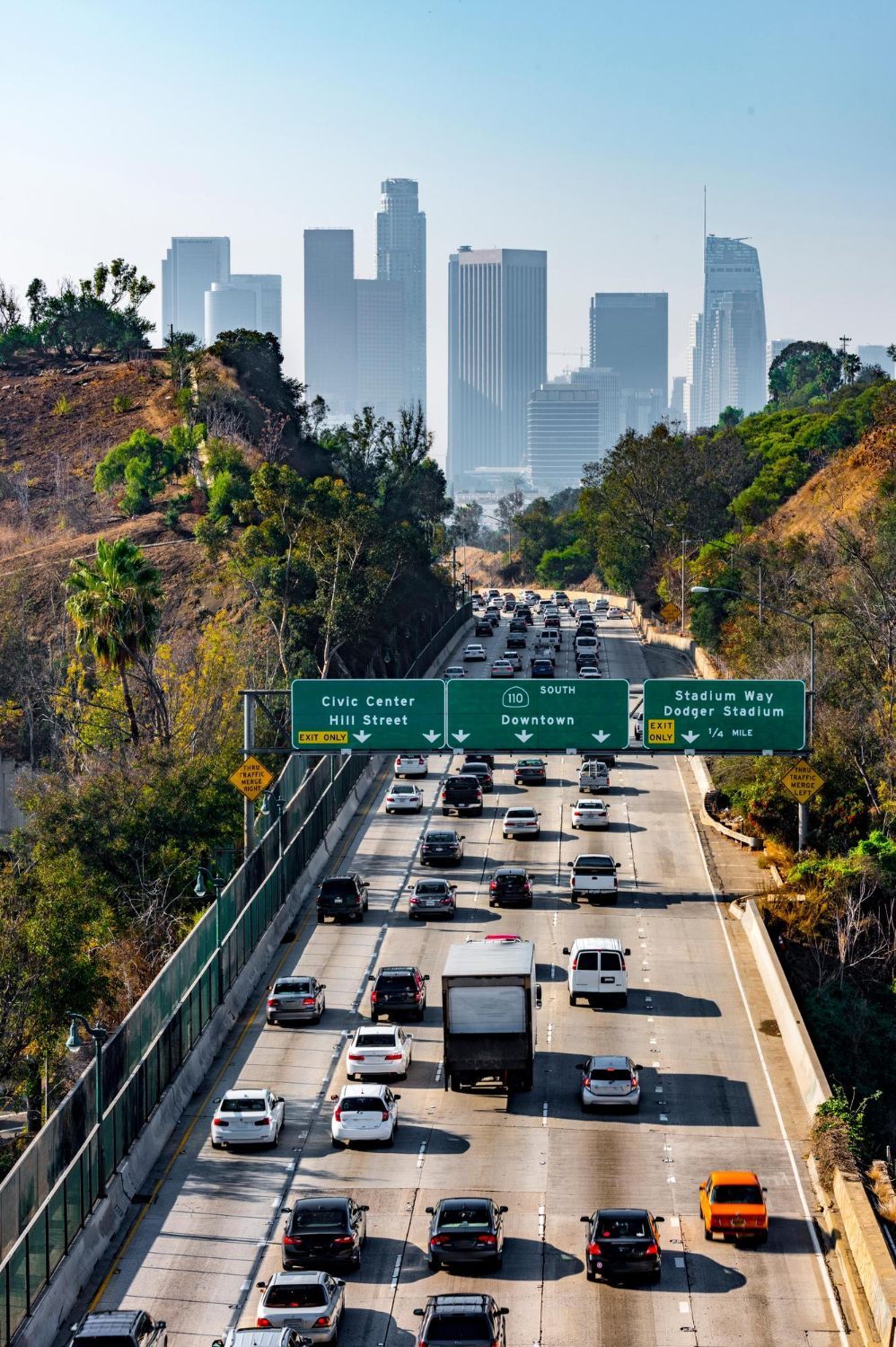 Busy multi-lane freeway leading toward a downtown skyline on a clear day