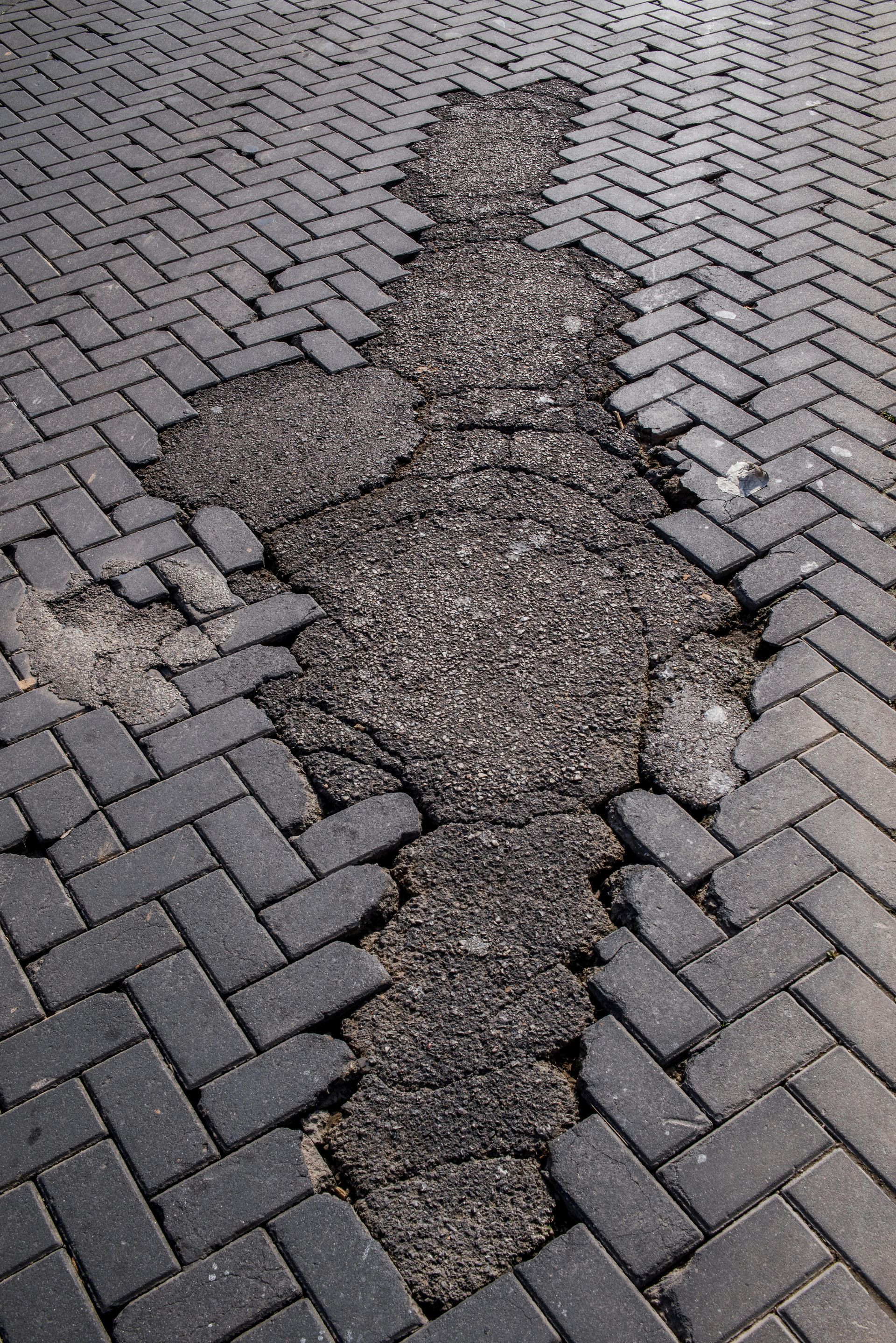 Damaged brick pavement with a large cracked and broken patch in the center