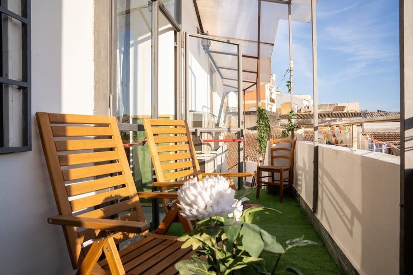 Sedie di legno su un piccolo balcone con erba sintetica e un grande fiore bianco. Giornata di sole, vista sulla città.