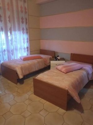 Due letti singoli in una stanza con pareti a righe rosa e grigie, biancheria da letto rosa e pavimento piastrellato color cuoio. Tra i letti c'è un comodino con una piccola statuetta.
