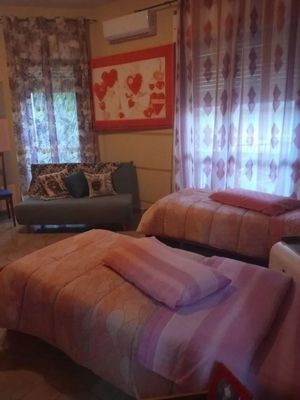 Una camera da letto con due letti ricoperti di lenzuola rosa. Un piccolo divano con cuscini decorativi e opere d'arte è appoggiato alla parete più lontana.