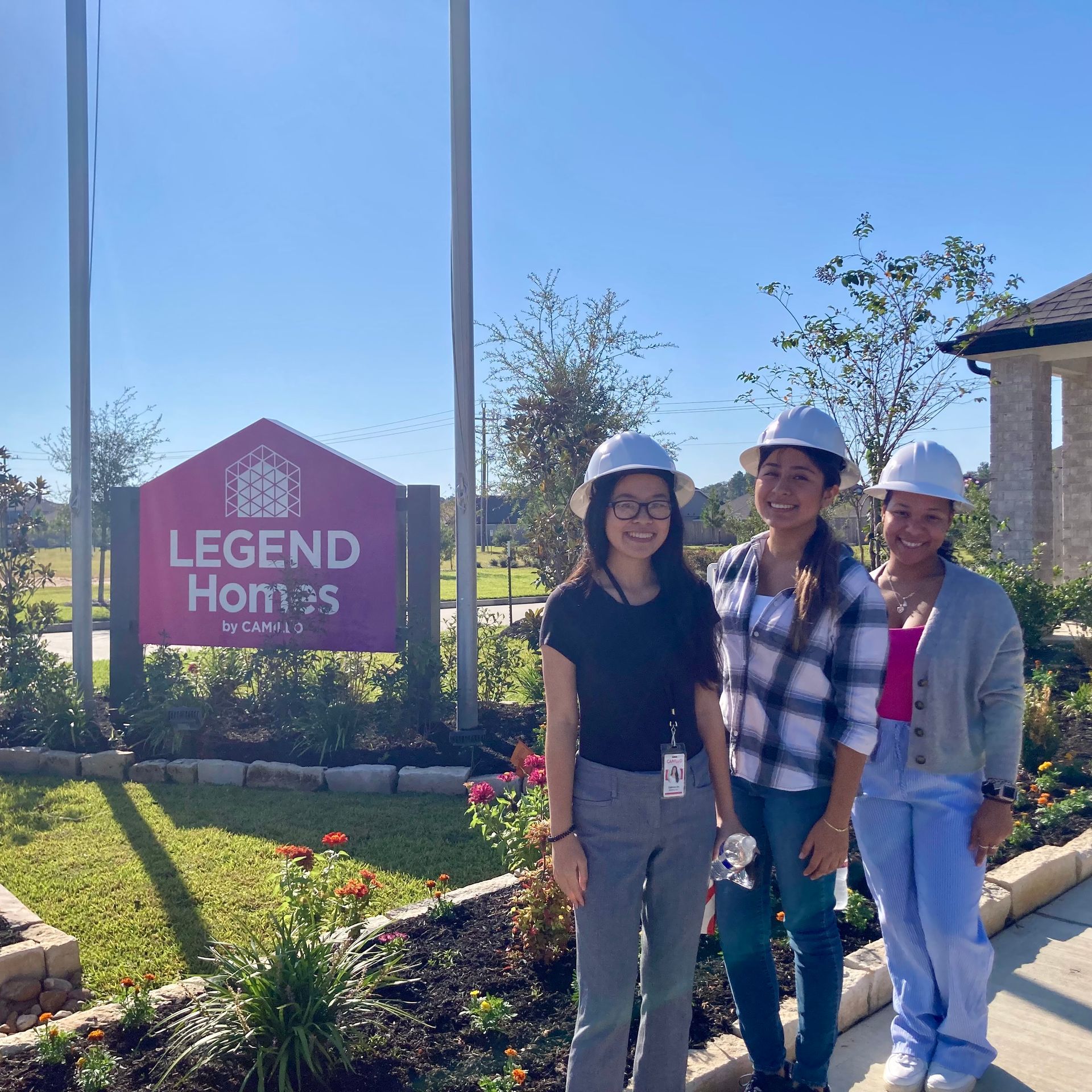 Three interns wearing hard hats at a model home site