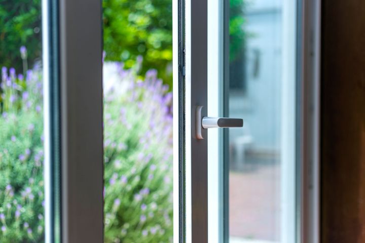 Partially open glass door with a silver handle, showing greenery outside.