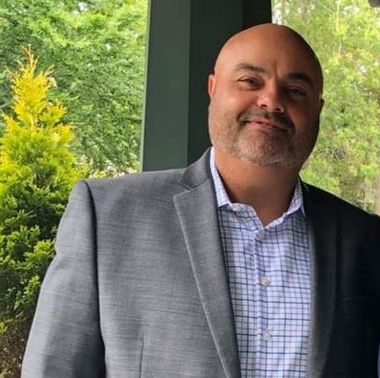 A man in a suit and plaid shirt is smiling for the camera.