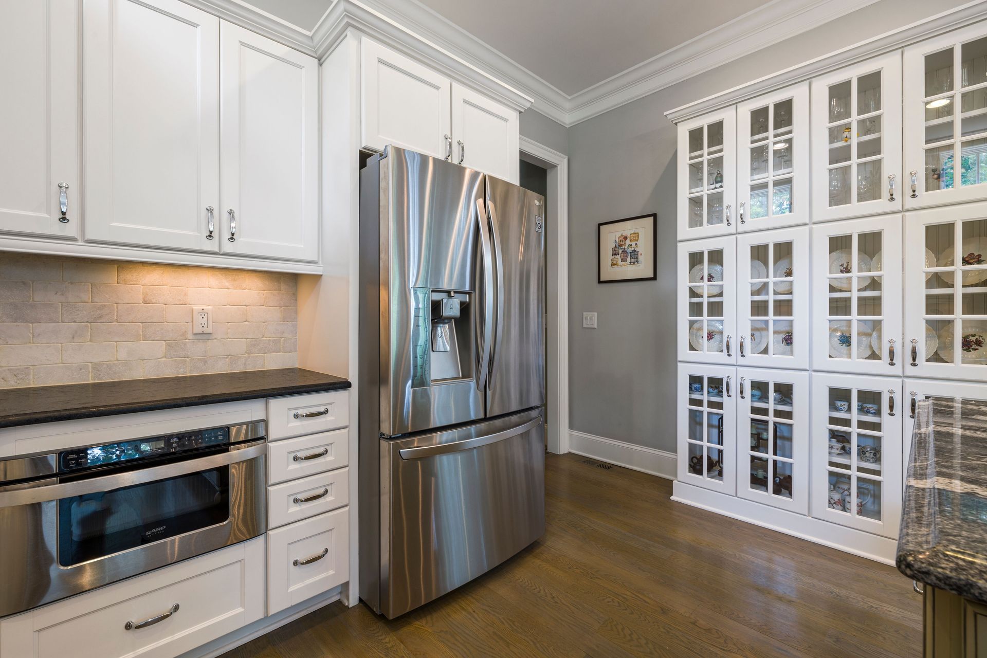 Modern kitchen with white cabinets, stainless steel appliances, and glass-front pantry doors