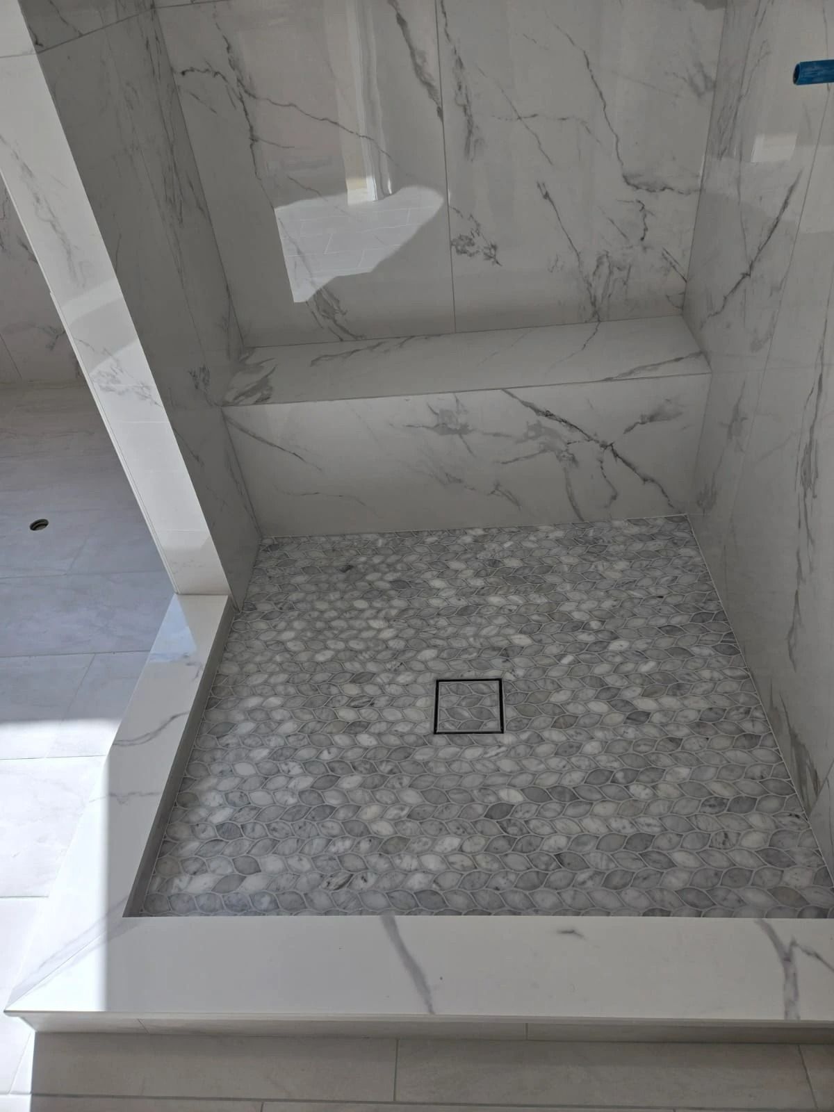 Small marble shower stall with a mosaic tile floor and square drain in the center.