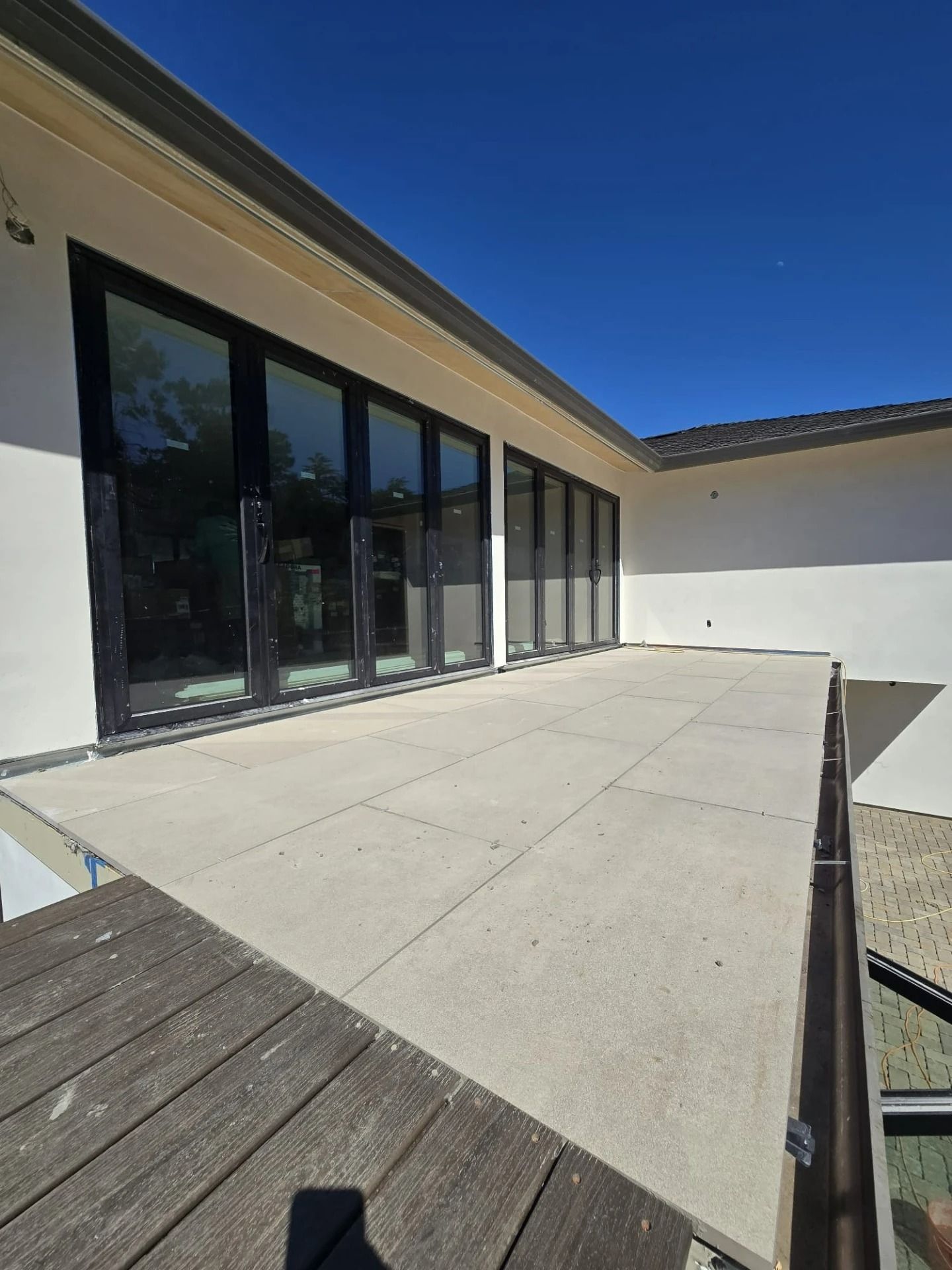 Modern patio with large glass doors, concrete surface, and wooden deck under a clear blue sky