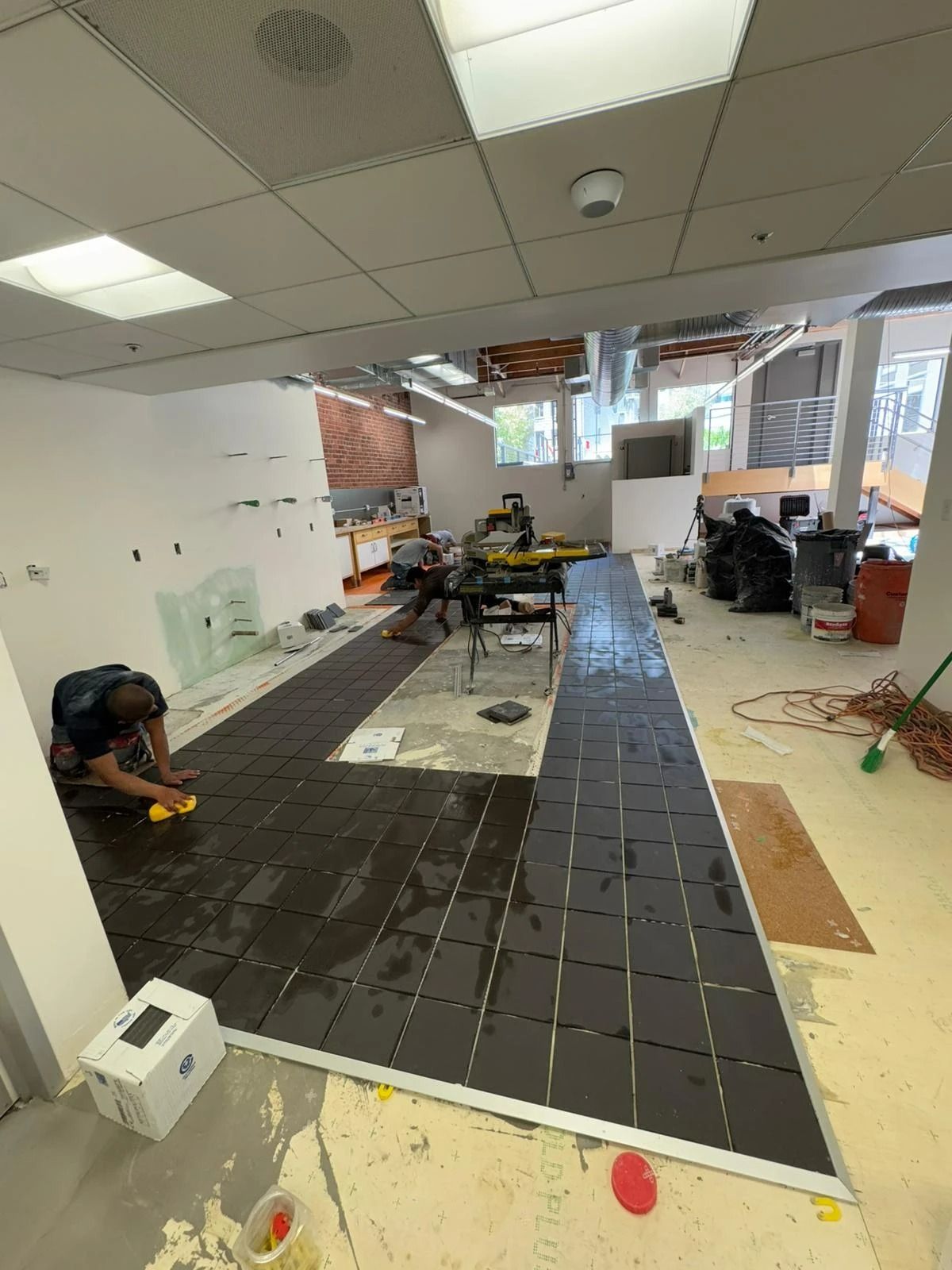 Indoor room with a long dark floor strip, scattered tools, chairs, and renovation materials.