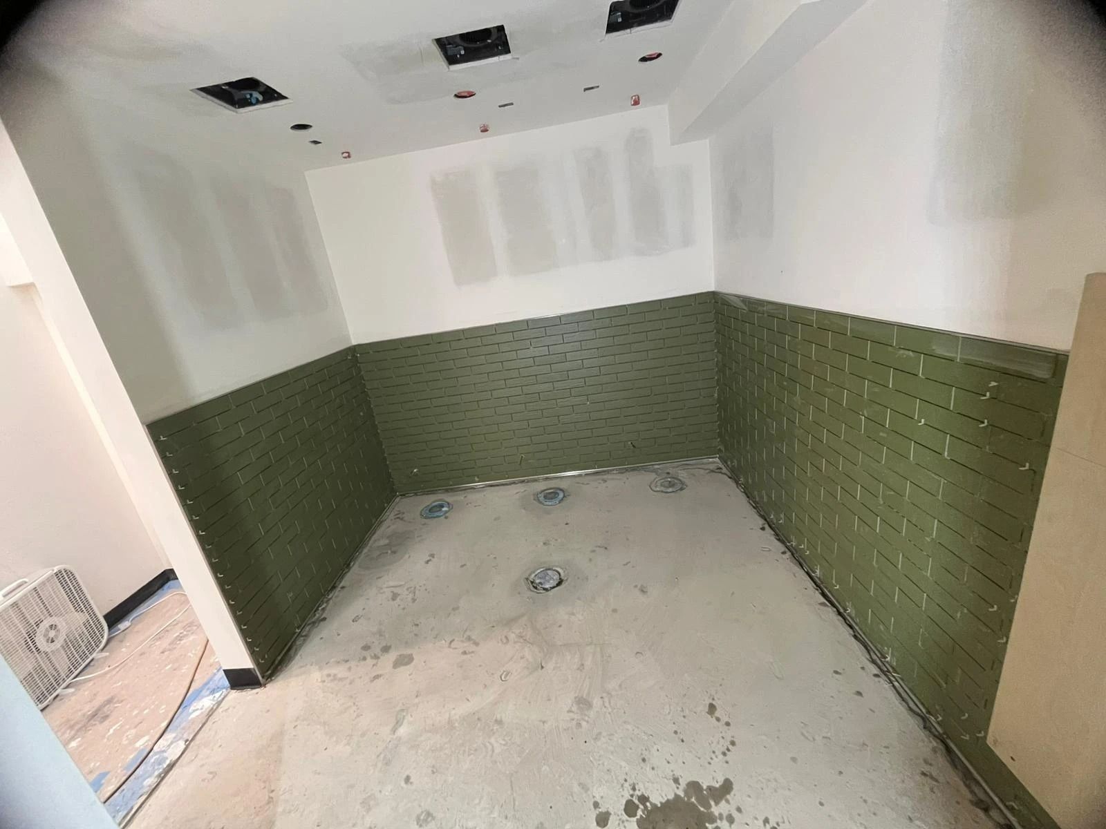 Empty tiled bathroom under renovation with green lower walls and unfinished ceiling outlets