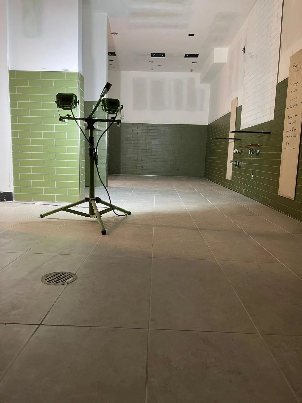 Empty hallway under construction with green wall tiles and a camera tripod in the center.