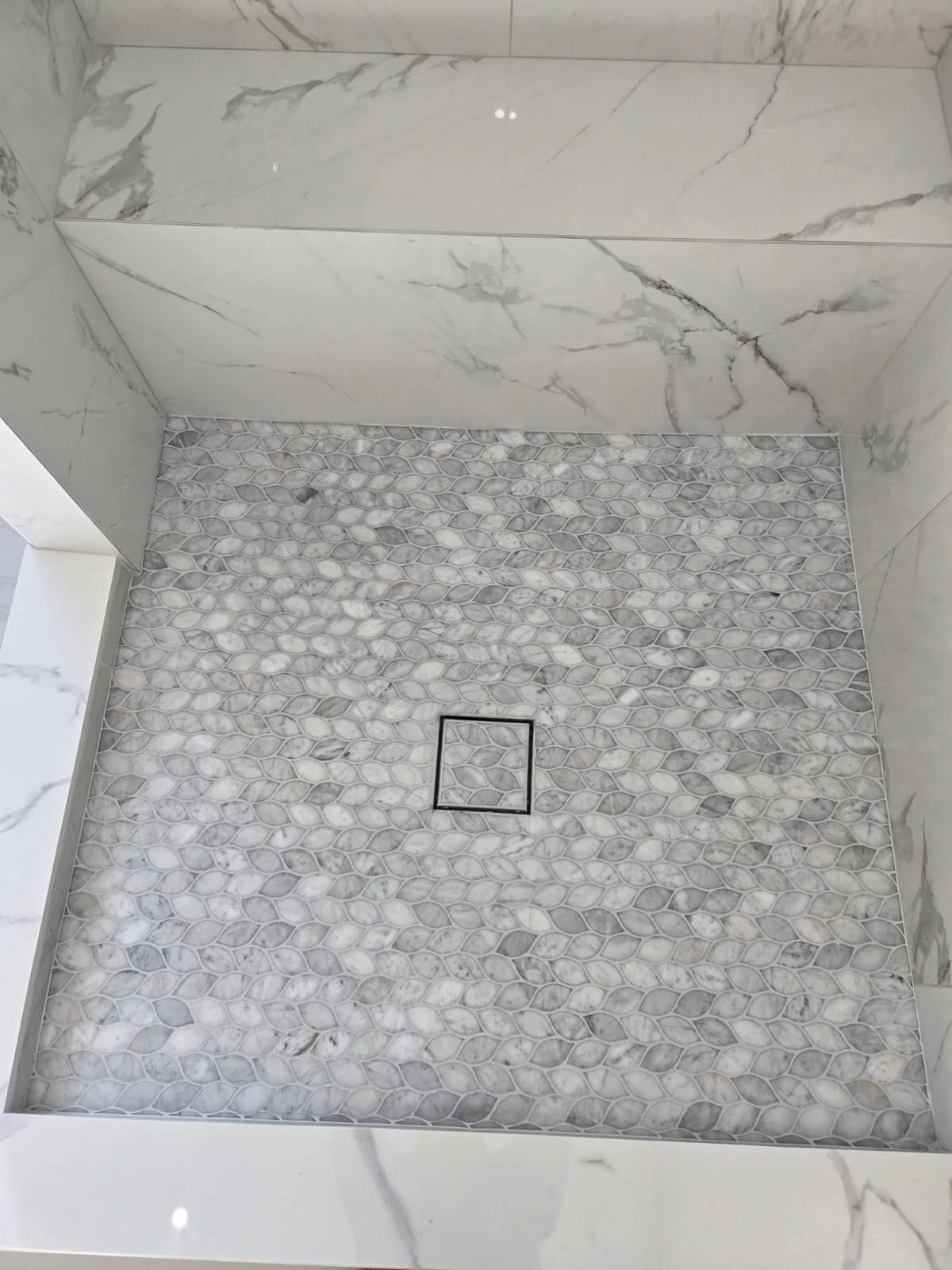 Empty marble-tiled shower floor with a central drain and gray pebble floor accent