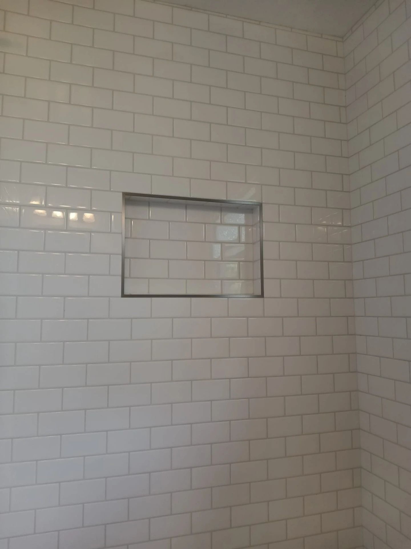 White tiled shower wall with a recessed niche shelf.