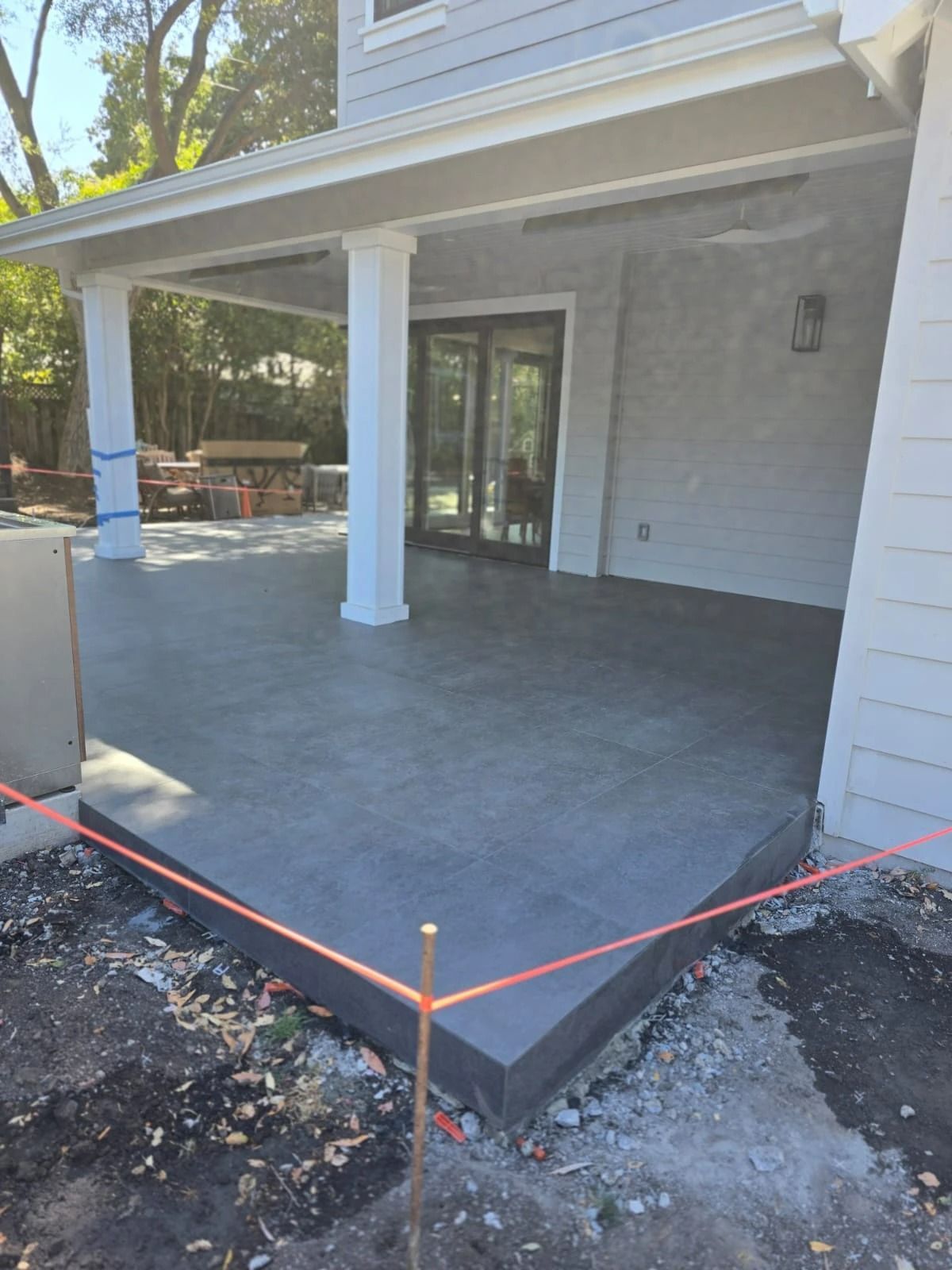 Covered front porch with gray tile floor, white columns, and sliding glass doors under construction