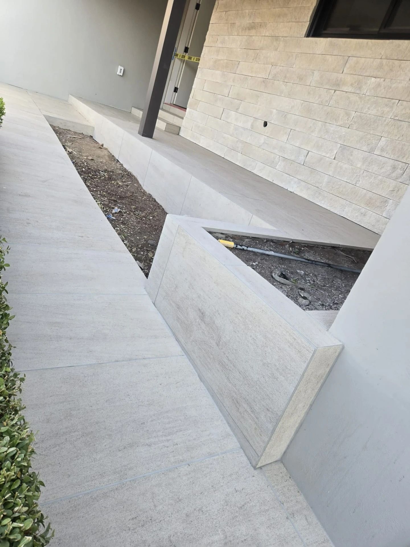 Modern concrete courtyard with raised planters and a white wall, viewed from a walkway