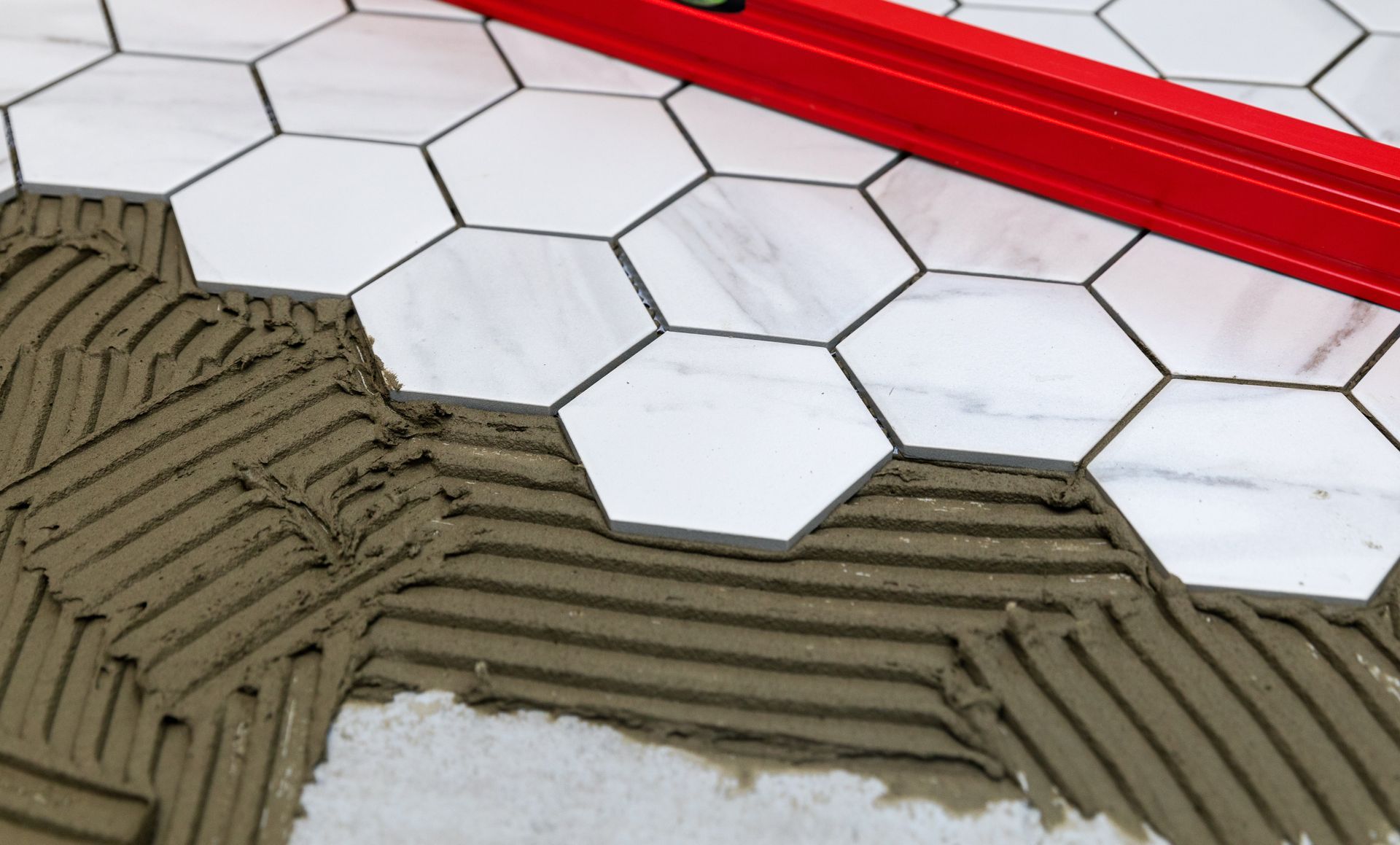 Hexagonal white tiles being set on adhesive mortar beside a red trim edge.