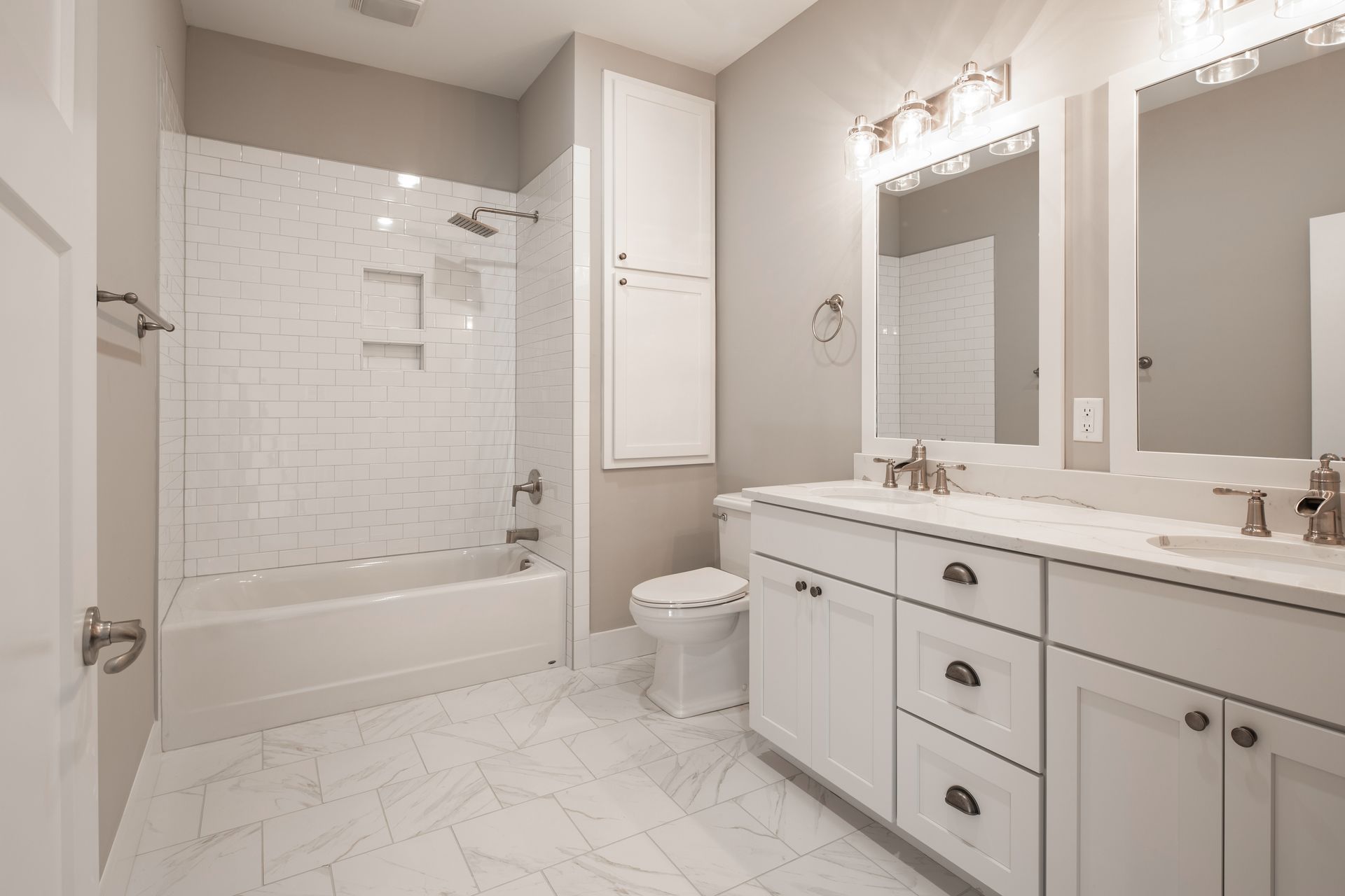 Bright white bathroom with a bathtub, double vanity, large mirror, and tiled floor