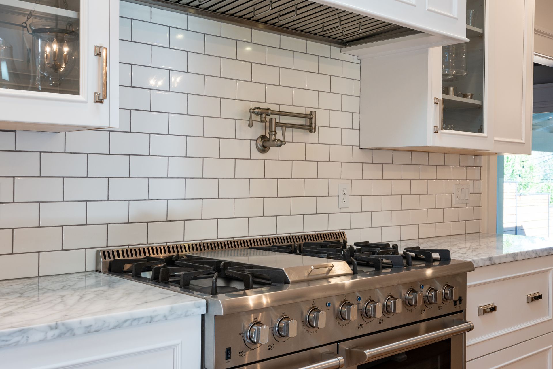 Modern kitchen with white subway tile backsplash, marble counters, and stainless steel gas range
