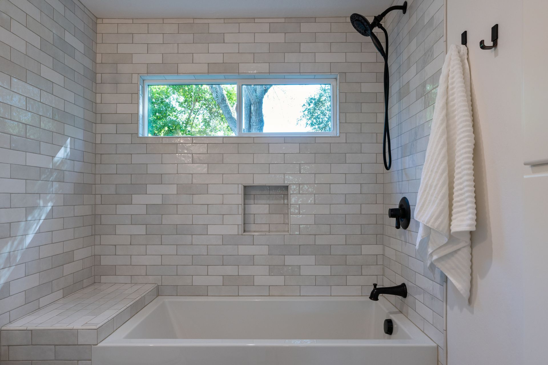 Bright white subway-tile bathroom with a tub, window, and black shower fixtures
