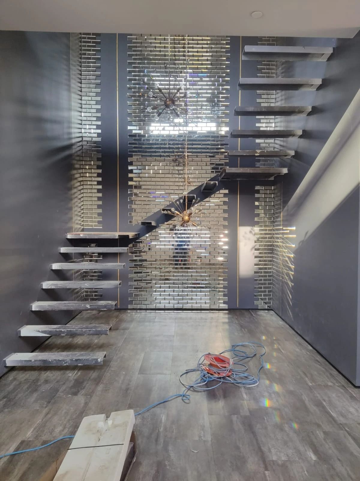 Modern gray interior with floating stairs, mirrored wall, and construction materials on the floor
