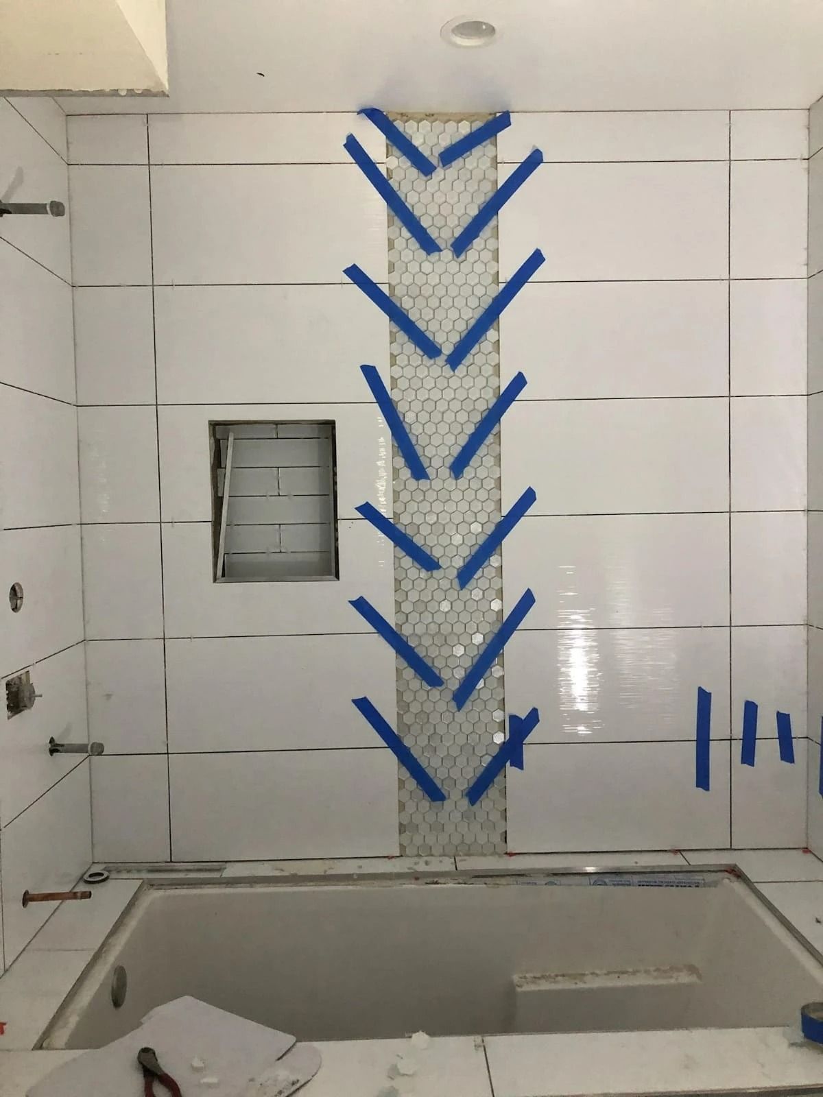 Bathroom under renovation with blue tape marking a tile layout above a bathtub.
