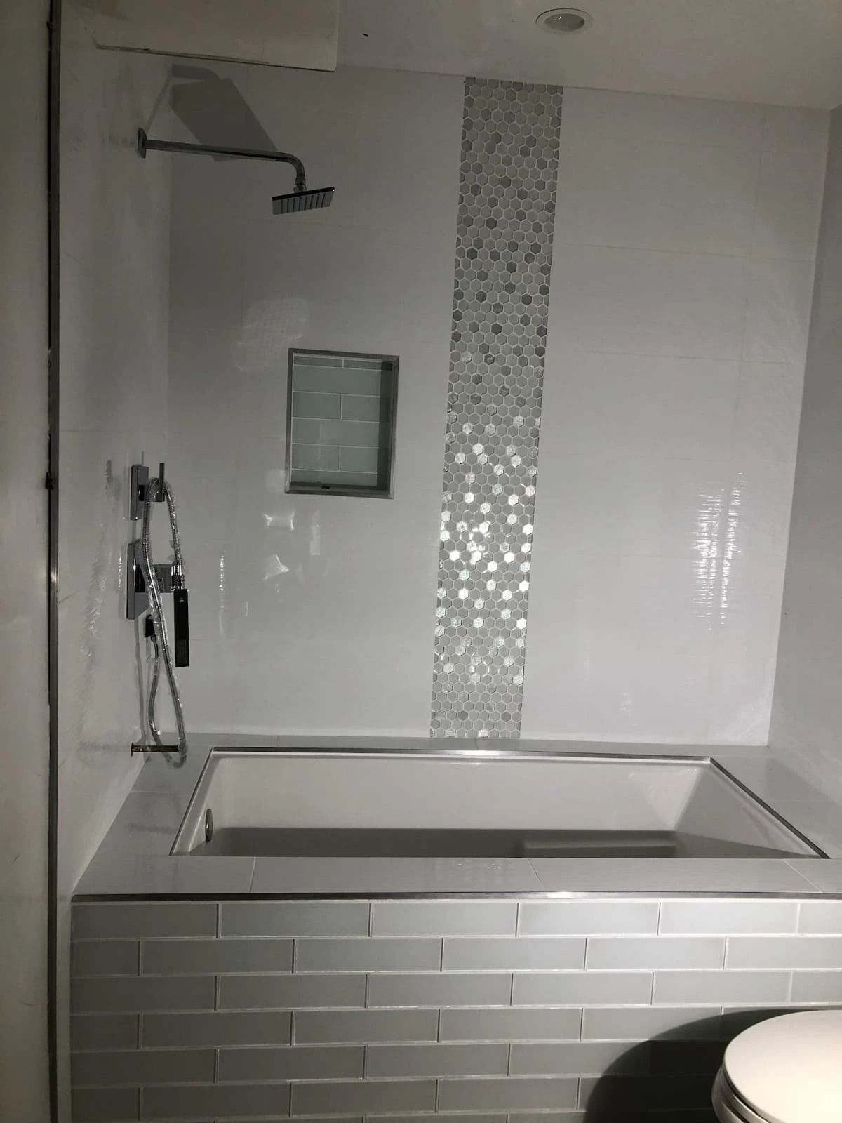 Modern bathroom with a white bathtub, wall showerhead, and tiled surround.