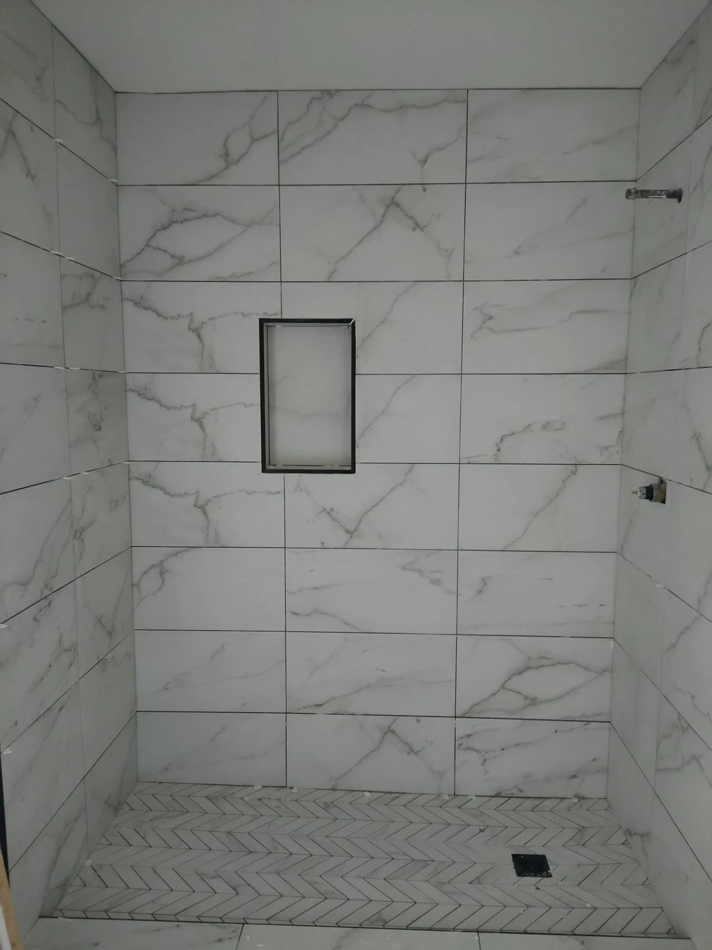 Marble-tiled shower with a recessed niche, built-in bench, and hexagonal tile floor drain.