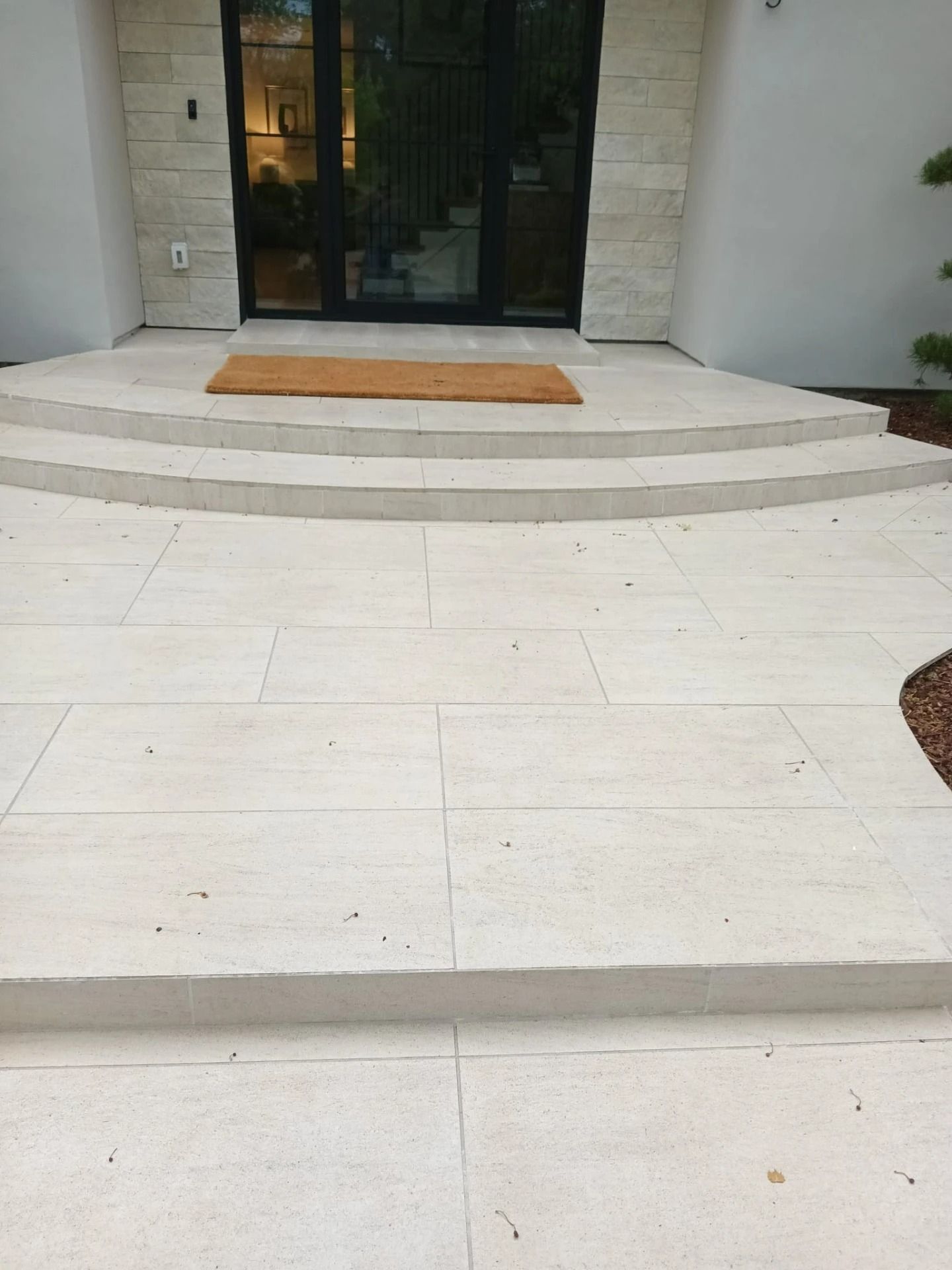 Front entrance with curved steps, tiled walkway, and a glass door under a porch.