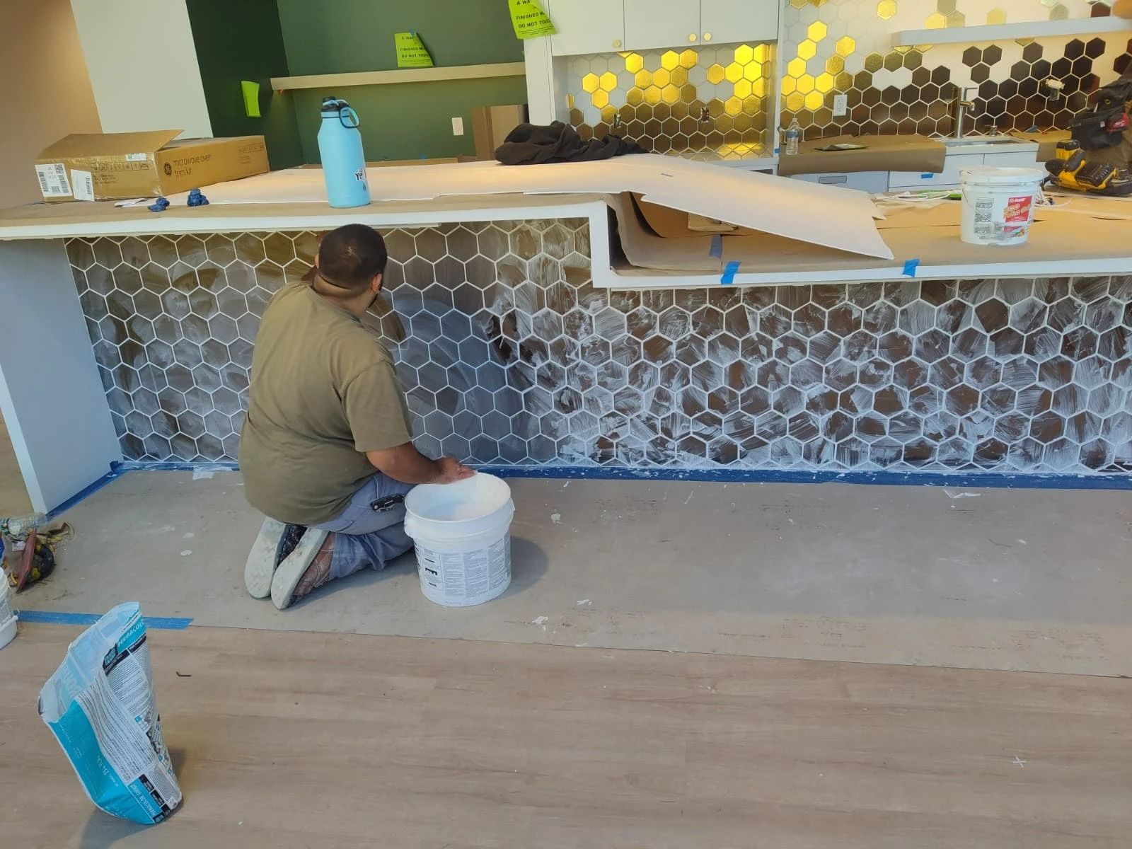 Person kneels on a floor, painting a counter front with a gray circular pattern in a room.