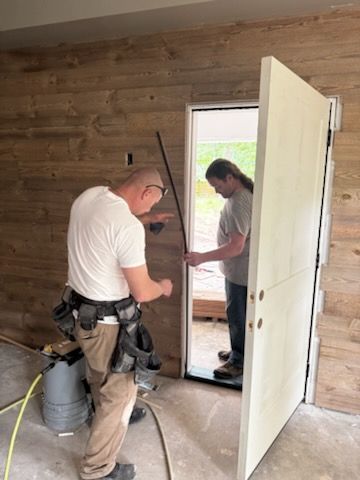 Two workers installing a white door in a wood-paneled room under construction
