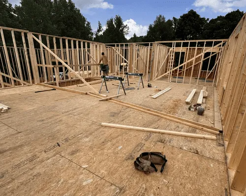 A person framing walls on the wooden subfloor of a house under construction.