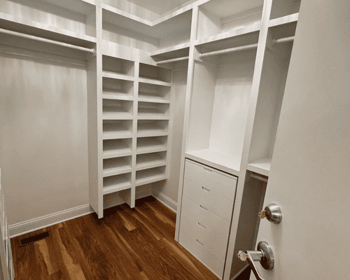 A modern white walk-in closet with built-in shelves, hanging rods, and a four-drawer unit on warm hardwood floors.