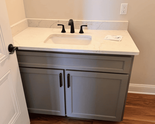 A gray bathroom vanity with a white marble countertop and black faucet against a light wall.