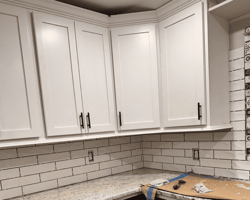White shaker kitchen cabinets installed above white subway tile backsplash and granite countertops.