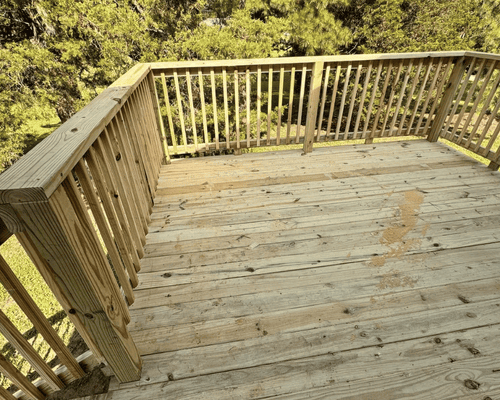 A wooden deck with railing overlooking trees on a sunny day.