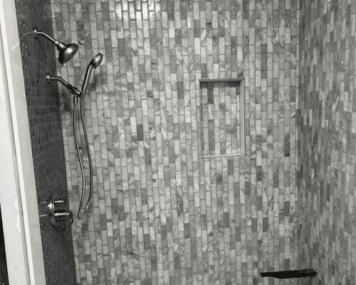 A modern shower with textured, light-colored rectangular wall tiles, a rainfall showerhead, and a recessed wall niche.