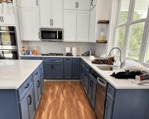 A kitchen with white upper cabinets, blue lower cabinets, a kitchen island, and stainless steel appliances.