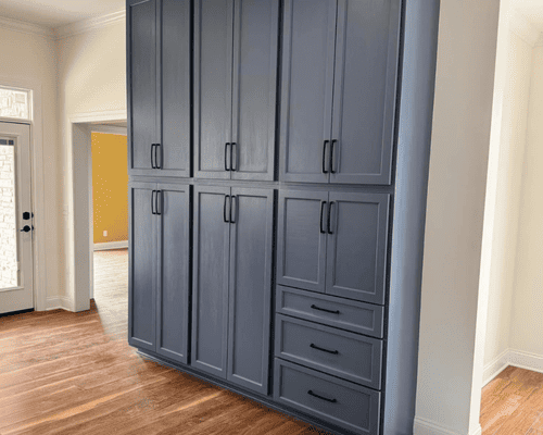 A large floor-to-ceiling slate-blue cabinet with double doors and three bottom drawers in a bright room with wood floors.