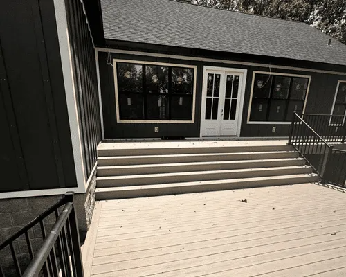 Dark gray exterior house wall with white French doors leading to a light-colored wooden deck with concrete steps.