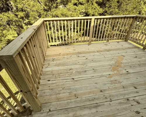 A high-angle view of a wooden deck with railing, overlooking a grassy yard with trees.