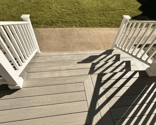 Gray composite deck stairs with white railings lead down to a concrete walkway and lawn.